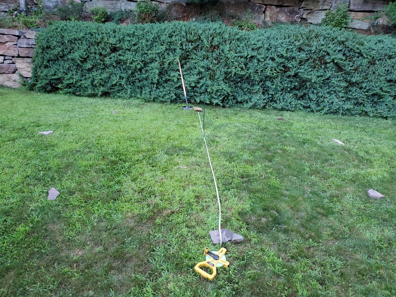 A stake and string marking the outline of a 14-foot circle in the backyard grass.